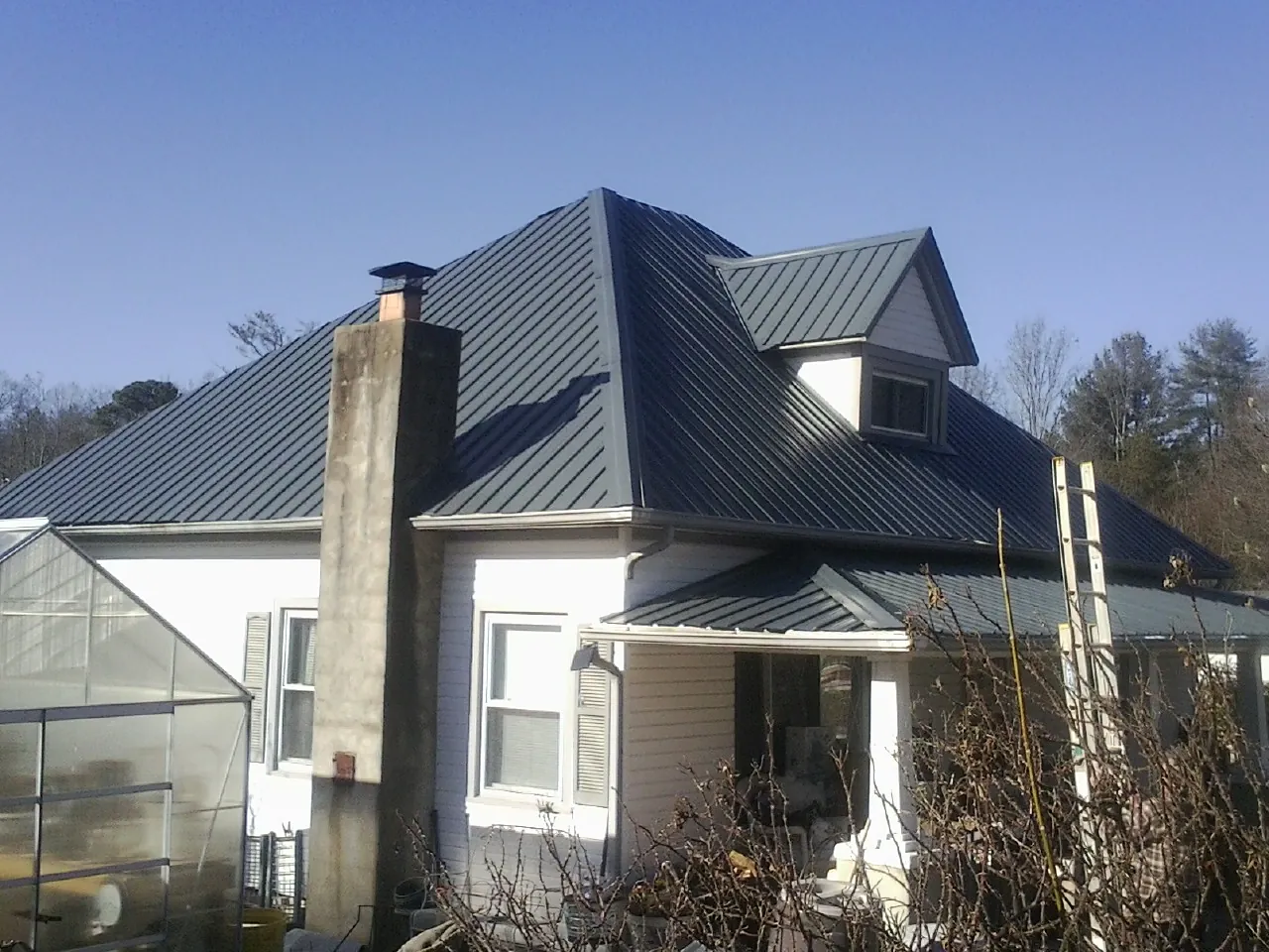 Dark blue standing seam metal roof on a white farmhouse with dormer — Slate & Tile Roof Repair by Roofing Brothers in Naturita
