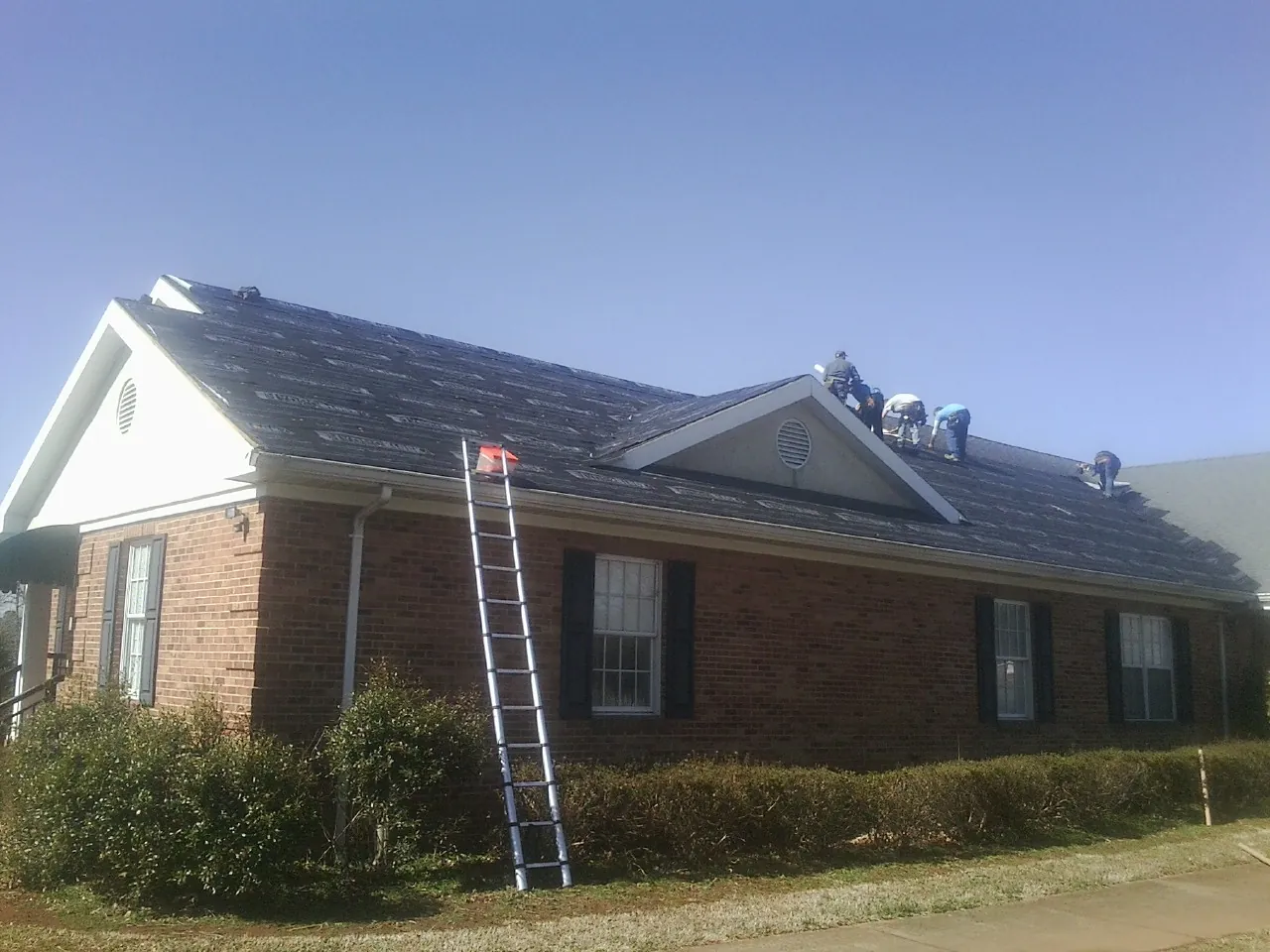 Crew tearing shingles off a brick ranch roof with a ladder set — Metal Roof Repair work by our crew in Naturita