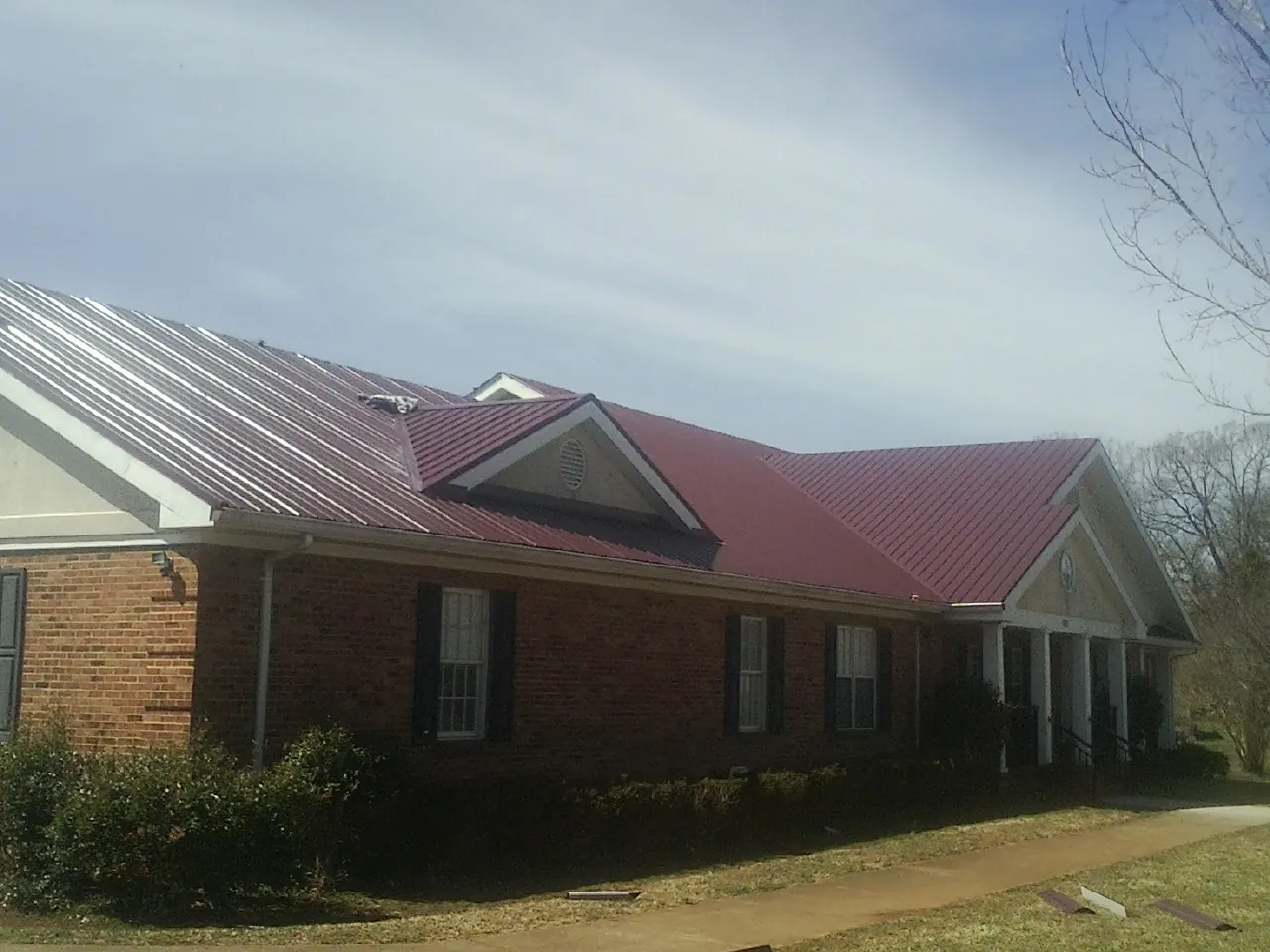 Red metal roof with gabled entries on a long brick building, from a Hail Damage Roof Repair job in Naturita