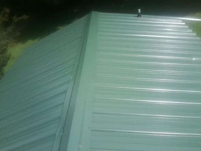 New green metal panels meeting at the ridge of a roof — Flat Roof Repair work by our crew in Naturita
