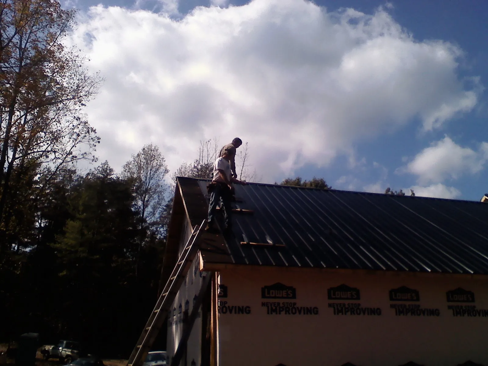 Roofer fastening dark metal panels high against a cloudy sky, from a Roof Inspection job in Naturita