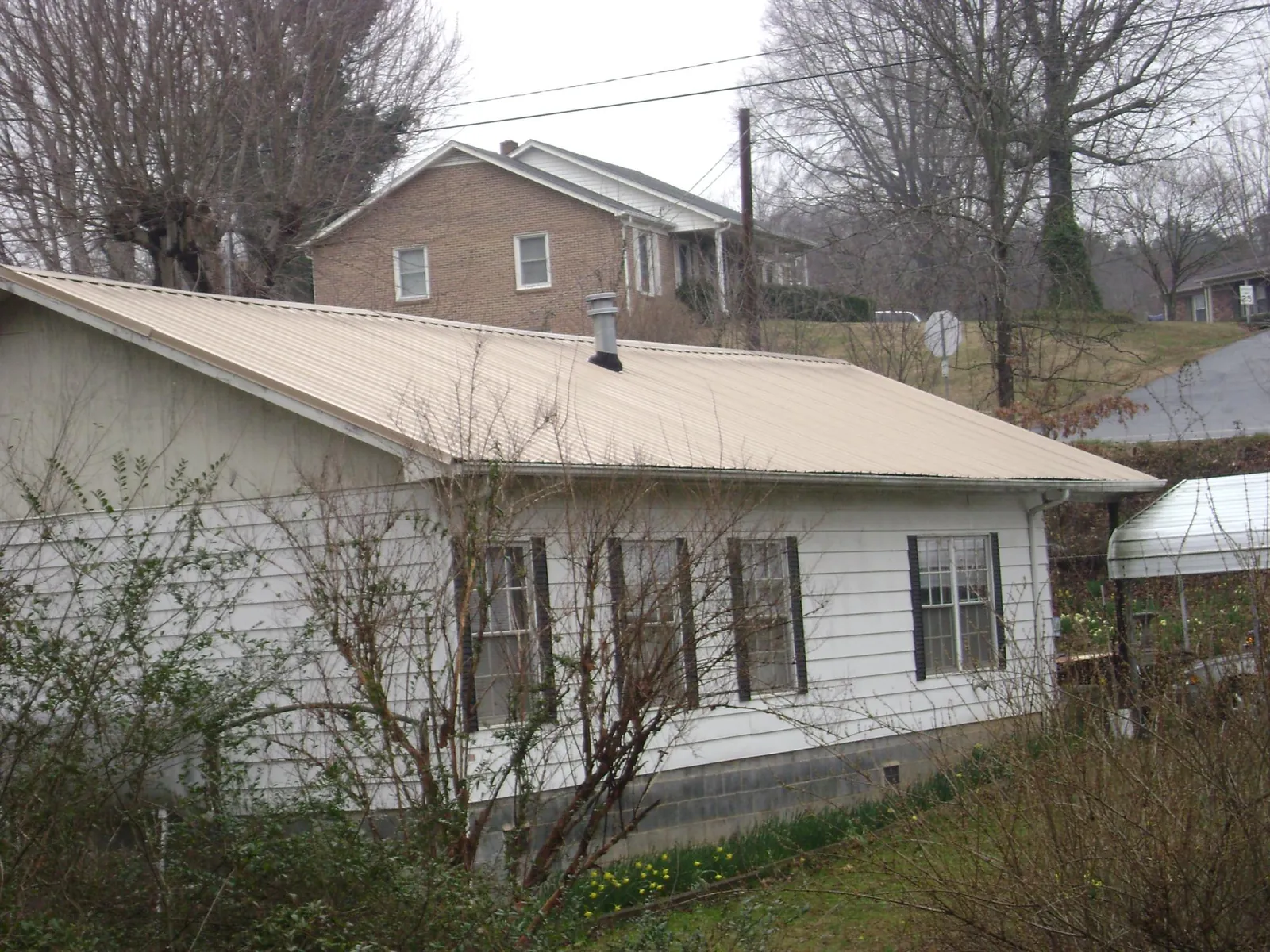 Tan metal roof on a white sided house set into a hillside — Commercial Roofing by Roofing Brothers in Naturita